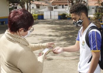 Funcionário higieniza mão de estudante na porta da escola em Jaguariúna: retomada Foto: Ivair de Oliveira/Divulgação