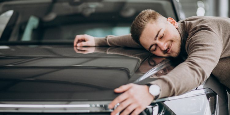 Young handsome man hugging a car in a car showroom