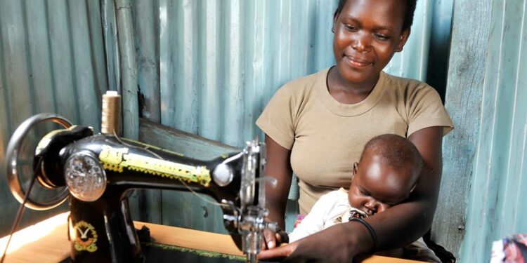 Mulher cuida do filho enquanto trabalha como costureira, no Quênia. Foto: Marcel Crozet/ONU