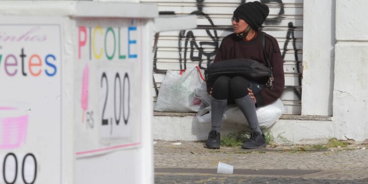 Mulher tenta se esconder do frio, perto de uma placa de venda de picolés. Fotos: Leandro Ferreira/Hora Campinas