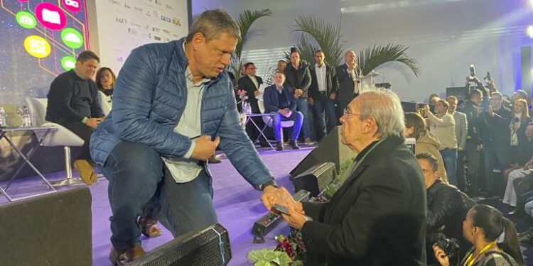 O governador Tarcísio de Freitas se ajoelha no palco para cumprimentar o presidente da ACL, Jorge Alves de Lima - Foto: Divulgação