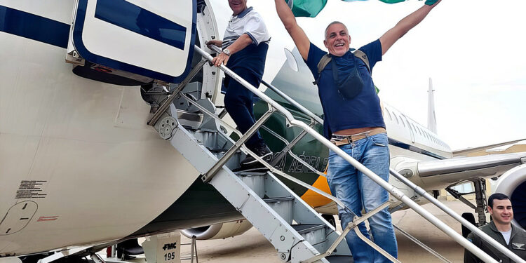 Repatriado em voo da FAB celebra a volta ao Brasil agitando a Bandeira Nacional durante o embarque - Imagem: Fotos Públicas/FAB/GOV