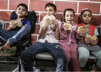 Crianças de famílias abrigadas numa escola da Unrwa em Gaza comem pão distribuído pelo Programa Mundial de Alimentos - Foto: PMA/Ali Jadallah