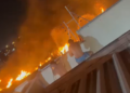 Com o fogo já no muro da casa, morador conta com a ajuda de mangueira para conter as chamas. Foto: Divulgação